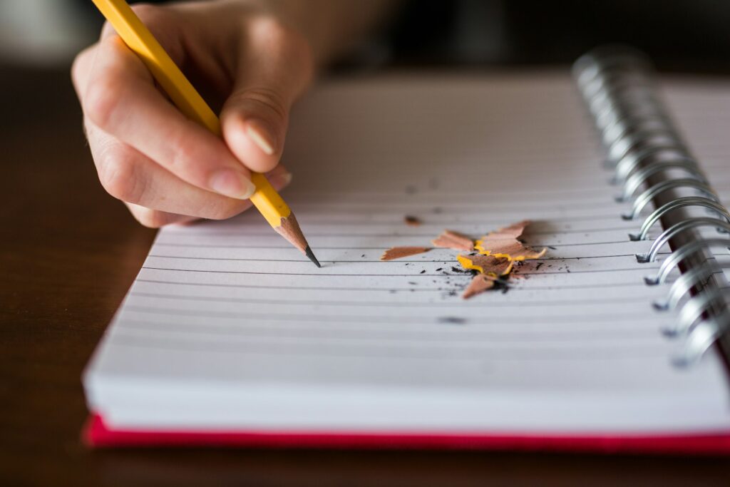 Close-up of a hand writing with a pencil in a spiral notebook
