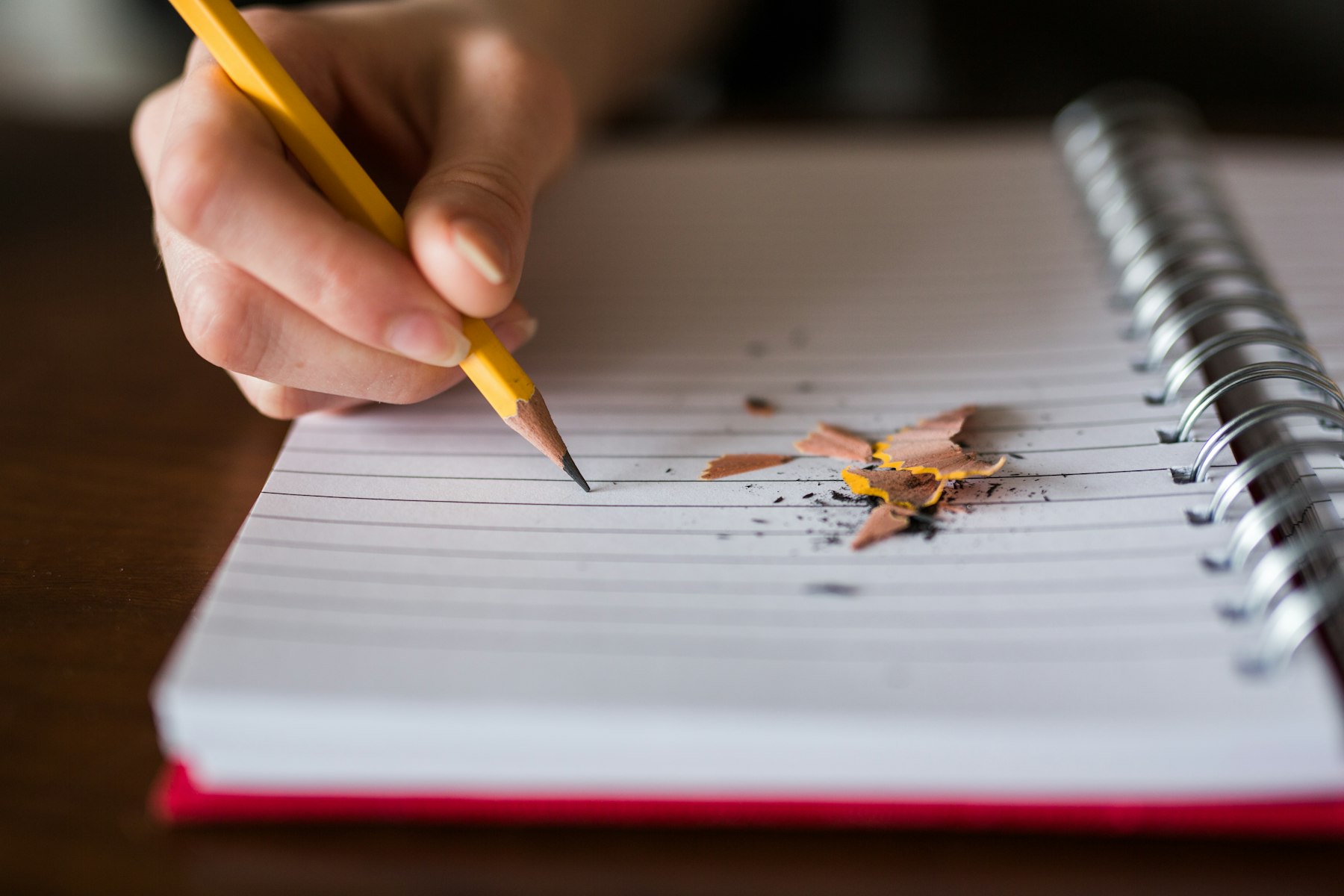 Close-up of a hand writing with a pencil in a spiral notebook