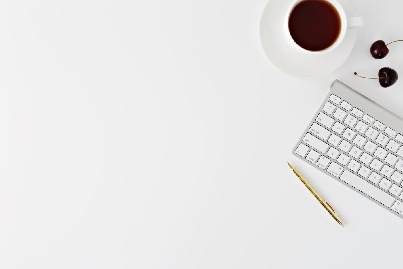 Minimal flat lay of a keyboard, coffee, and pen on a white desk