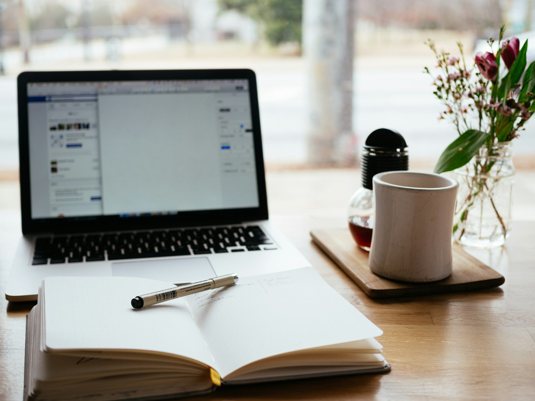 Laptop and open notebook on a wooden desk, set up for writing a blog post