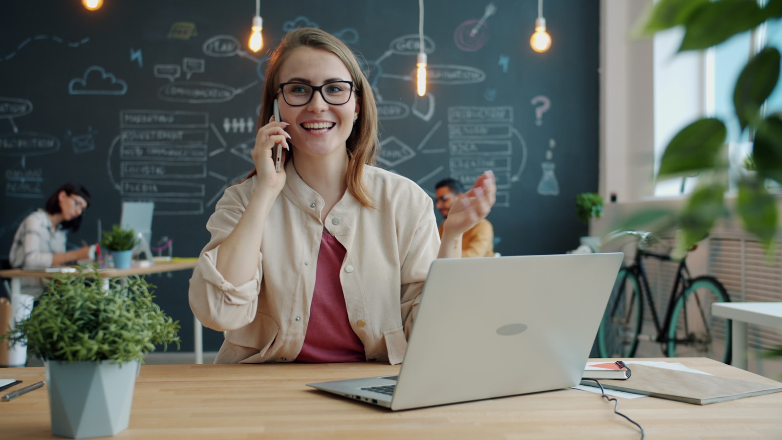 Smiling woman on a phone call at her desk with a laptop, discussing project goals