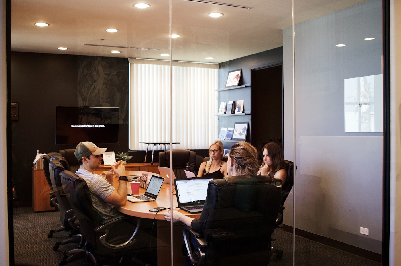 Marketing team collaborating around a table with laptops in a glass-walled office