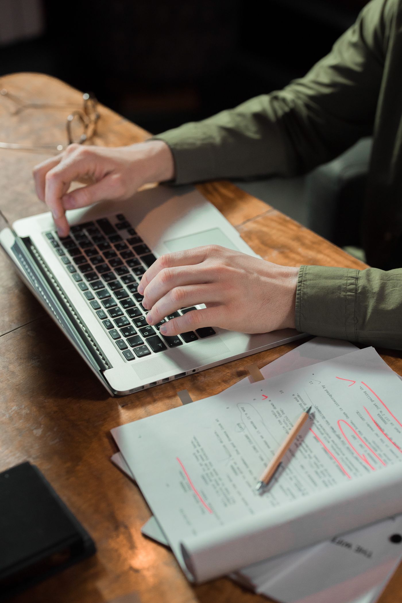 Hands typing at a laptop next to a printed page marked up in red pen, the kind of editing pass a content audit's update bucket leads to