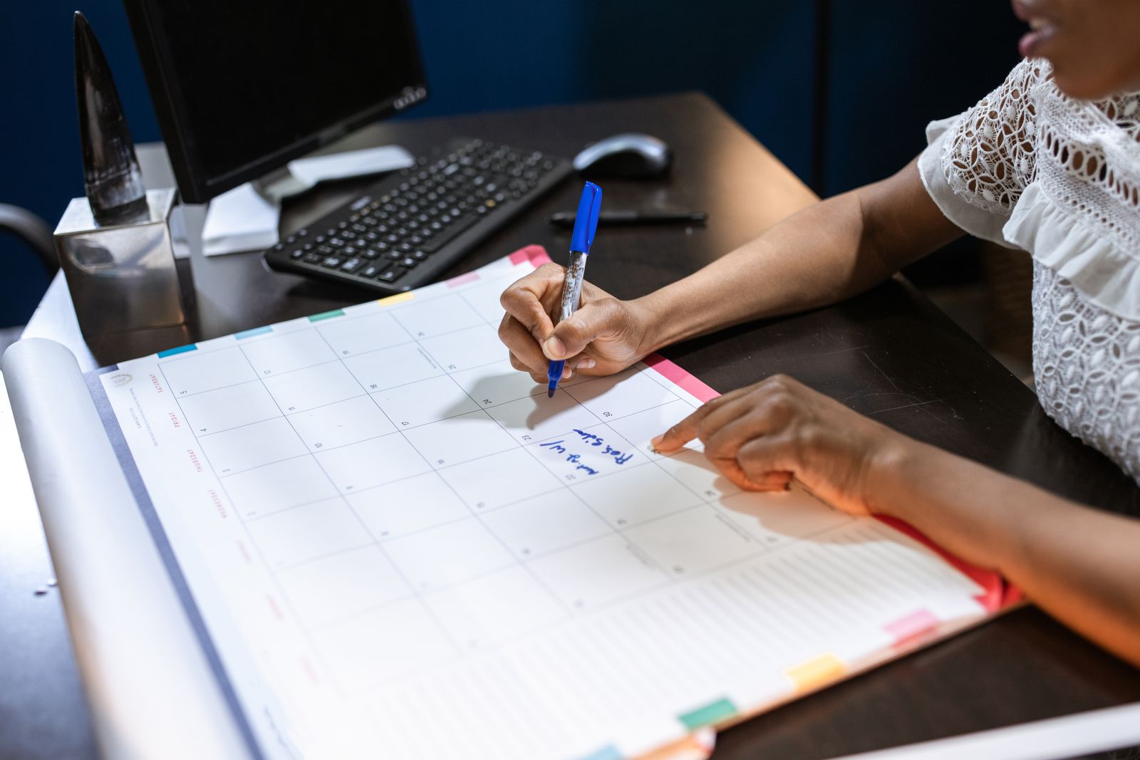 Woman writing a note into a large monthly wall calendar at her desk