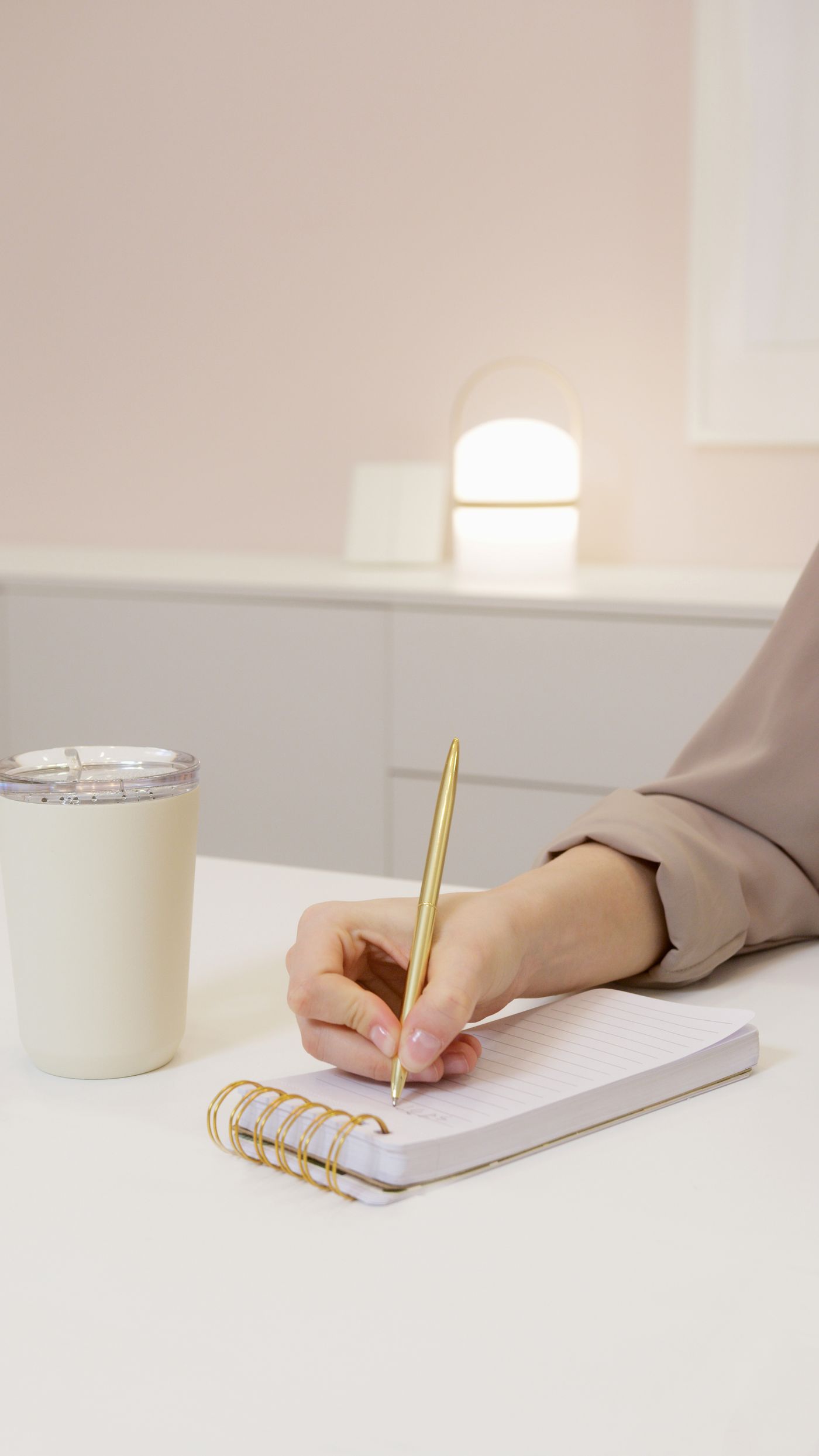 Hand holding a gold pen, writing an outline in a spiral notebook next to a coffee cup