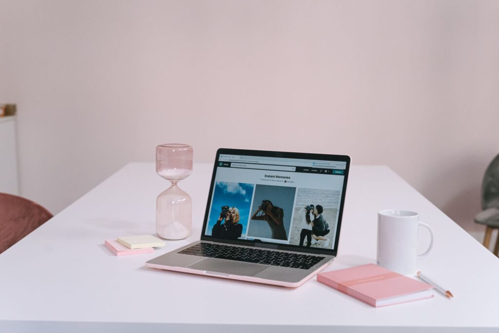 Pink hourglass next to an open laptop on a white desk, symbolizing how long SEO takes to show results