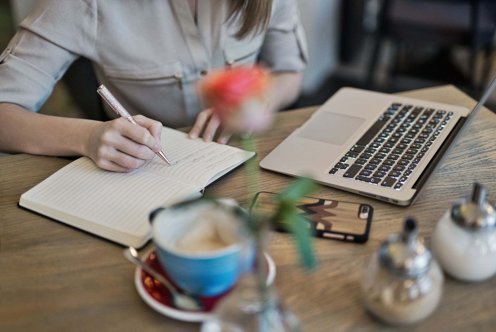 Writer drafting notes by hand next to an open laptop and coffee, planning a blog post