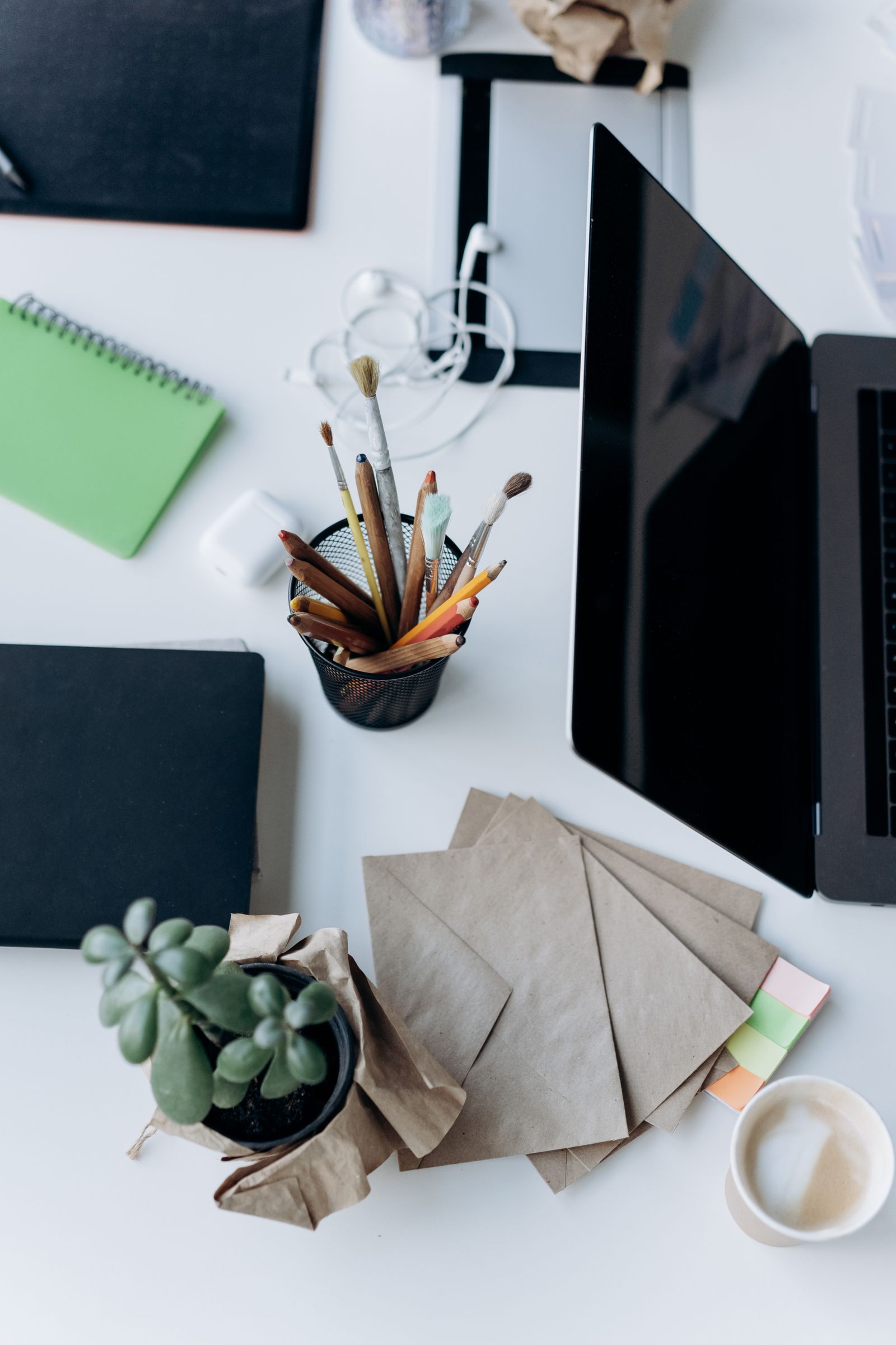 Fanned kraft envelopes next to a closed laptop and a small succulent on a white desk