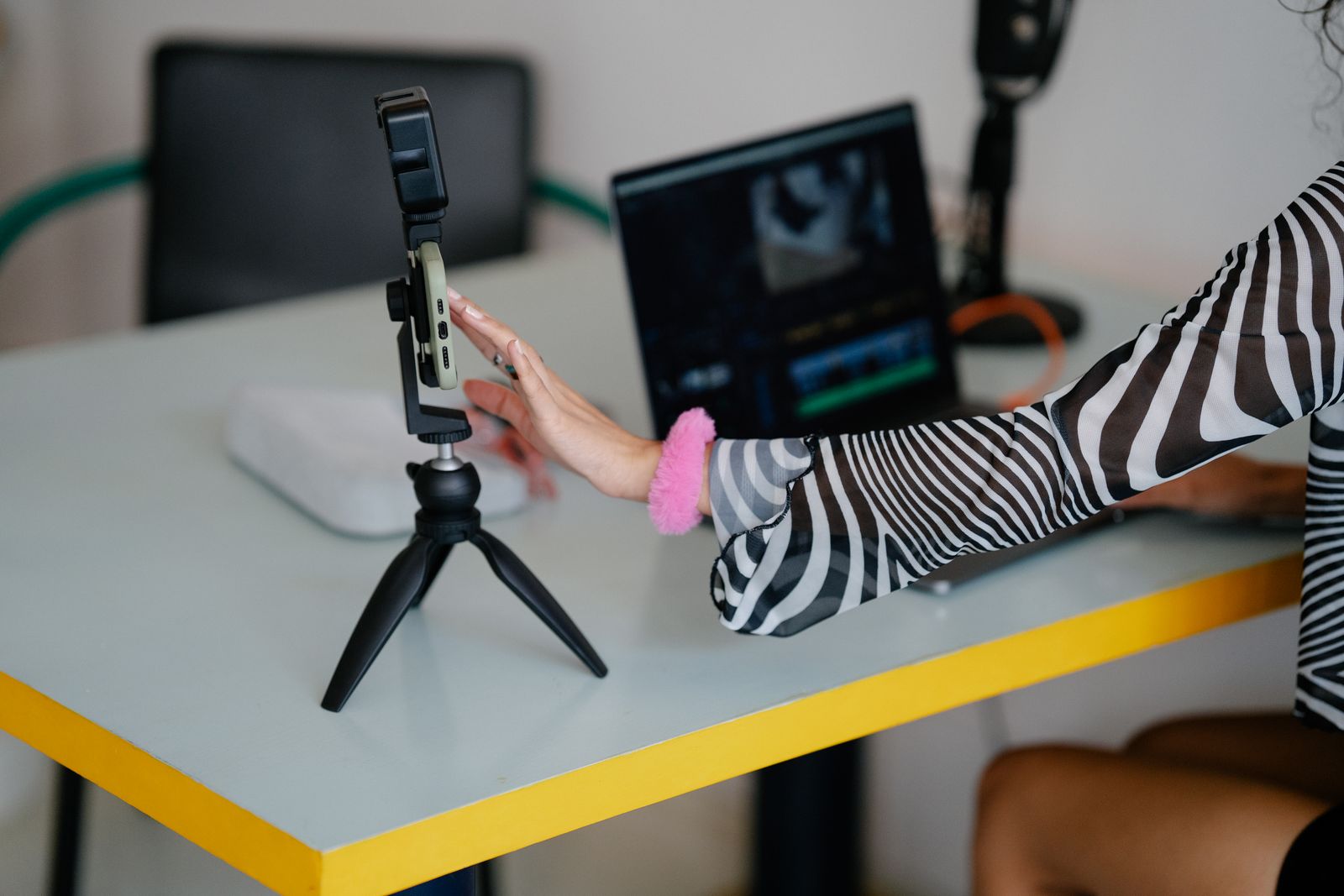 A phone mounted on a tripod next to a laptop showing video editing software, set up for repurposing content across formats